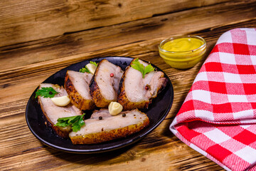 Slices of baked pork belly, garlic and parsley on a black plate