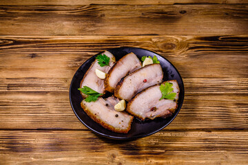 Slices of baked pork belly, garlic and parsley on a black plate