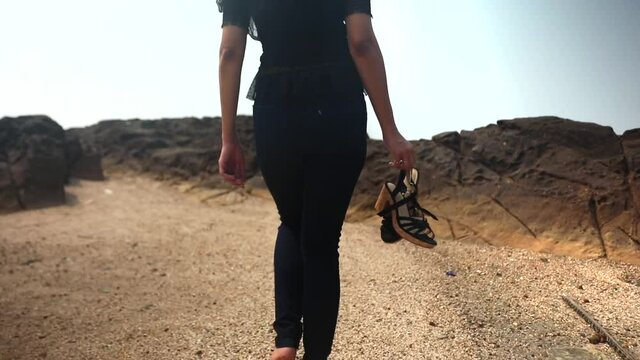 indian skinny girl walking on beach in black cloths without sandel in hand