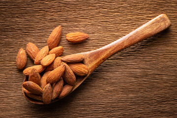 roasted salted almonds in wooden spoon on rustic natural wood texture background, harmony brown tone