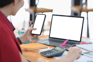 Businesswoman using mobile phone and working with laptop computer at office.