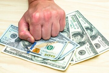 a man holds a stack of hundred-dollar bills lying on the table with his fist