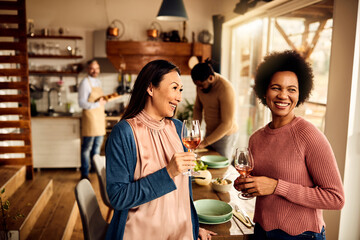 Happy women drink wine and talk while their husbands are preparing food in the kitchen.