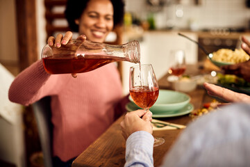 Close-up of African American woman pours wine into friend's glass at the dining room table.