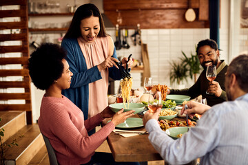 Happy Asian woman have fun while serving pasta to her friends during lunch at home.