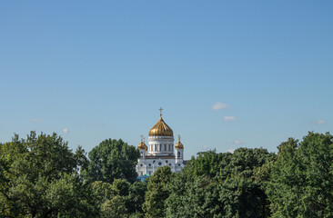 MOSCOW, RUSSIA-AUGUST, 4, 2021: the white-stone Cathedral of Christ the Savior with a golden dome against the background of a cloudless blue sky and green lush foliage of trees and a copy space