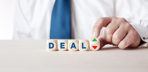 Business person is turning a wooden cube with the arrows next to the word deal. The decision or dilemma to accept or reject a business deal