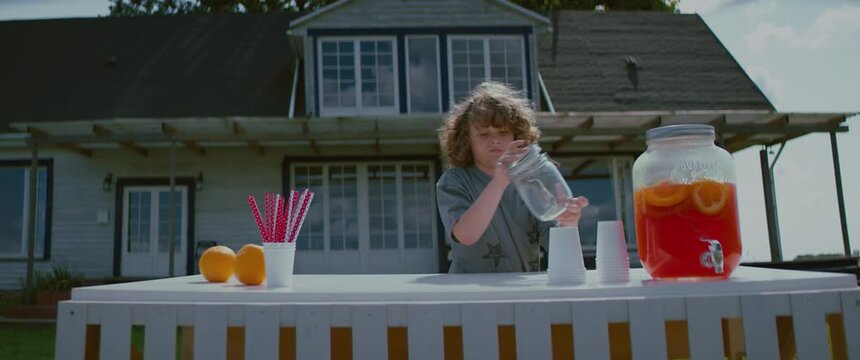 Cute Little Caucasian Kid Boy Opens Lemonade Stand On A Lawn In Front Of His House. Shot With 2x Anamorphic Lens