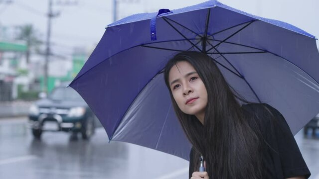Young asian woman with a long black hair looking out through the road for bus or taxi, public transportation service, asian living in rainy season, tropical climate change, hands collecting raindrops