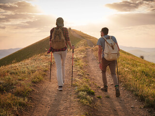 A couple of happy young hikers backpacking on a beautiful rocky trail on a warm, sunset evening. The concept of family travel and adventure. view from behind. Travel lifestyle. © Seleznov_Molchanova