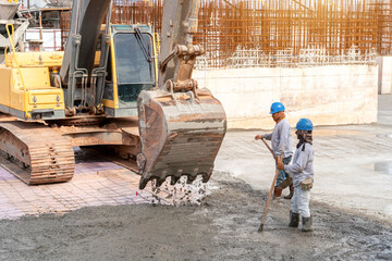 Construction worker with excavator heavy machine for Concrete pouring during commercial concreting floors of building at construction site