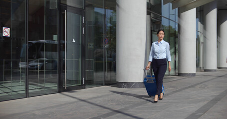 Asian businesswoman in formal wear walk outdoors carrying suitcase