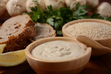 Tahini and sesame seeds in wooden bowls on wooden table.