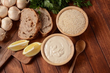 Tahini and sesame seeds in wooden bowls on wooden table.