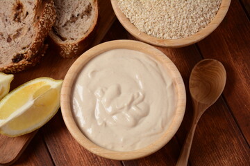 Tahini and sesame seeds in wooden bowls on wooden table.