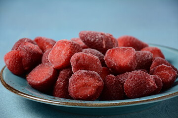 Frozen strawberries in blue plate on blue background