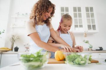 Mommy teaching her teen daughter to cook vegetable salad in kitchen