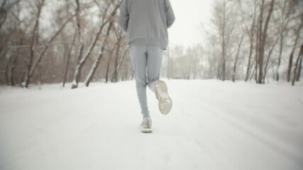 Sportsman legs runs in sportswear and sneakers in winter park, back view, closeup. Man jogging winter park during snowfall. Concept healthy lifestyle