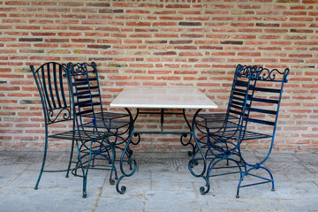 Elegant black metallic chairs and one white table near a red bricks wall in a garden in a sunny spring day, in Bucharest, Romania .