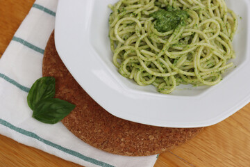 Plate of italian Spaghetti pasta with Pesto sauce on wooden table with fresh basil leaves 