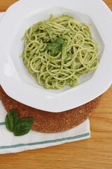 Plate of italian Spaghetti pasta with Pesto sauce on wooden table with fresh basil leaves 