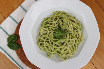 Plate of italian Spaghetti pasta with Pesto sauce on wooden table with fresh basil leaves 