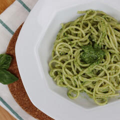 Plate of italian Spaghetti pasta with Pesto sauce on wooden table with fresh basil leaves 
