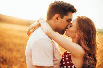 Close up photo of a ginger woman with freckles kissing her lover in a sunny field of wheat embracing