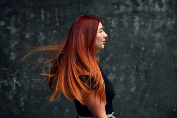 Side view of a redhead model with curly hair on a gray background looking straight.