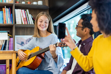 group of students having fun in college, friends of different ethnicities singing and playing guitar, young blonde woman filmed with her smartphone by the African woman