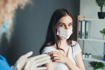Adorable woman is looking at camera while taking the corona virus vaccine wearing a mask at the...