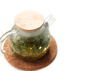 Misted glass teapot with a spring on a cork stand on a white background.