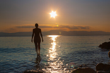 Fototapeta premium silhouette of a woman entering the sea at sunset
