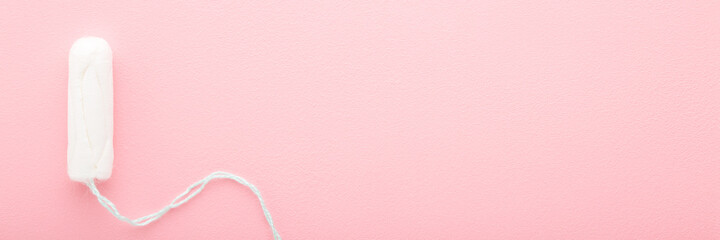 One new white sanitary tampon on light pink table. Wide banner background. Pastel color. Closeup....