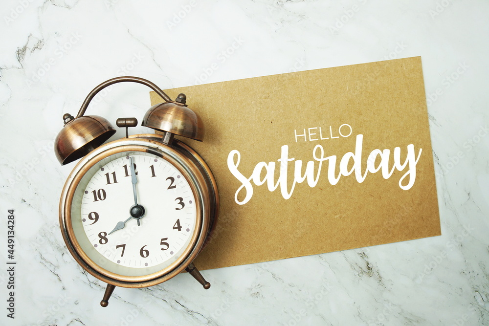 Wall mural hello saturday typography text on paper card with alarm clock on marble background