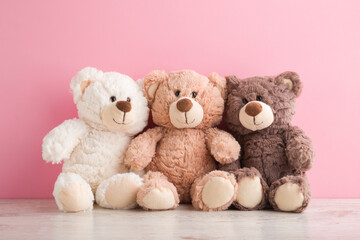 Smiling white, light brown and dark brown teddy bears sitting on table at pink wall background....