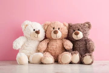 Fotobehang Smiling white, light brown and dark brown teddy bears sitting on table at pink wall background. Pastel color. Togetherness and friendship concept. Front view. Closeup. © fotoduets