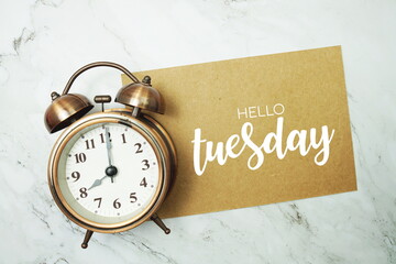 Hello Tuesday typography text on paper card with alarm clock on marble background
