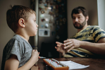 cute little caucasian boy doing his mental arithmetic homework with father sitting next to him at...