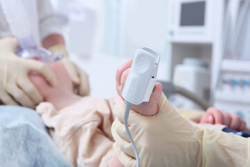 A device for measuring the concentration of oxygen in the blood on a child's finger. Preparing for surgery. The child is under anesthesia. Oxygen face mask. Life saving. The child is out of focus.