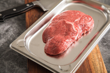 Rinder Steak roh auf Edelstahl Schale mit Küchenmesser, Holzbrett und Stein Hintergrund dunkel