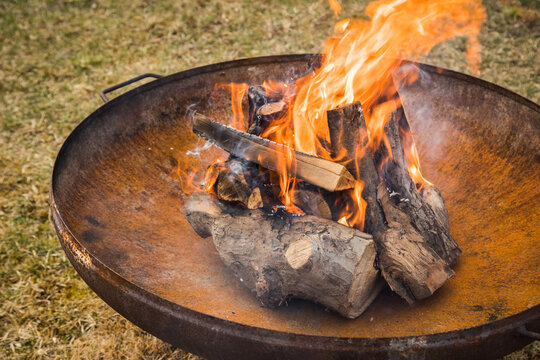 Feuer von Lagerfeuer mit trockenen Holz Scheiten in Metall Feuerschale draussen im Garten auf Wiese
