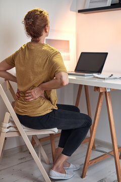 Woman working on a laptop at home and having problems with hips, back and stomack ache.