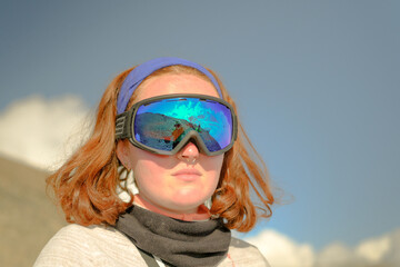Portrait of a red-haired woman in a ski mask. Tourist climber on the background of mountains.