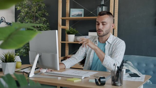Young professional architect is studying construction plan looking at paper and computer screen working at home alone. Engineering and freelance work concept.