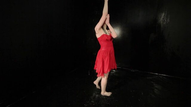 Woman in a red dress whirls while dancing while standing in the water.