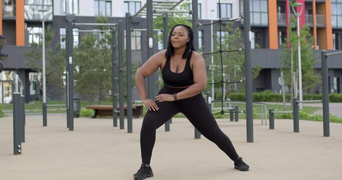 african fat overweight woman in black sportswear stretching body, warm up muscles before running or workout outdoors, doing exercises. weight loss, sport, healthy lifestyle, fitness concept
