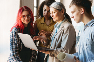 Mature teacher using laptop while talking with her students in art school