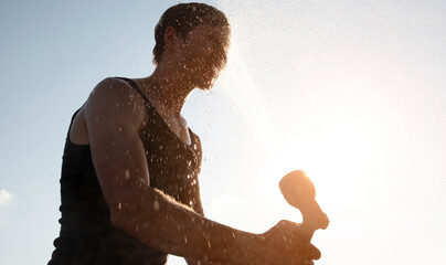 Man is refreshing himself with water spray gun in the hot summer day at the backyard