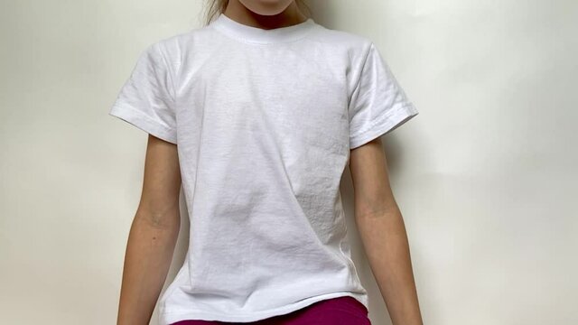 The girl tries to keep her back straight . Closeup view of a young woman wearing blank white T-shirt seating in front of grey background